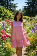 A sleeveless pink dress with a darker pink floral pattern, hanging on a black hanger against a white closet wall.